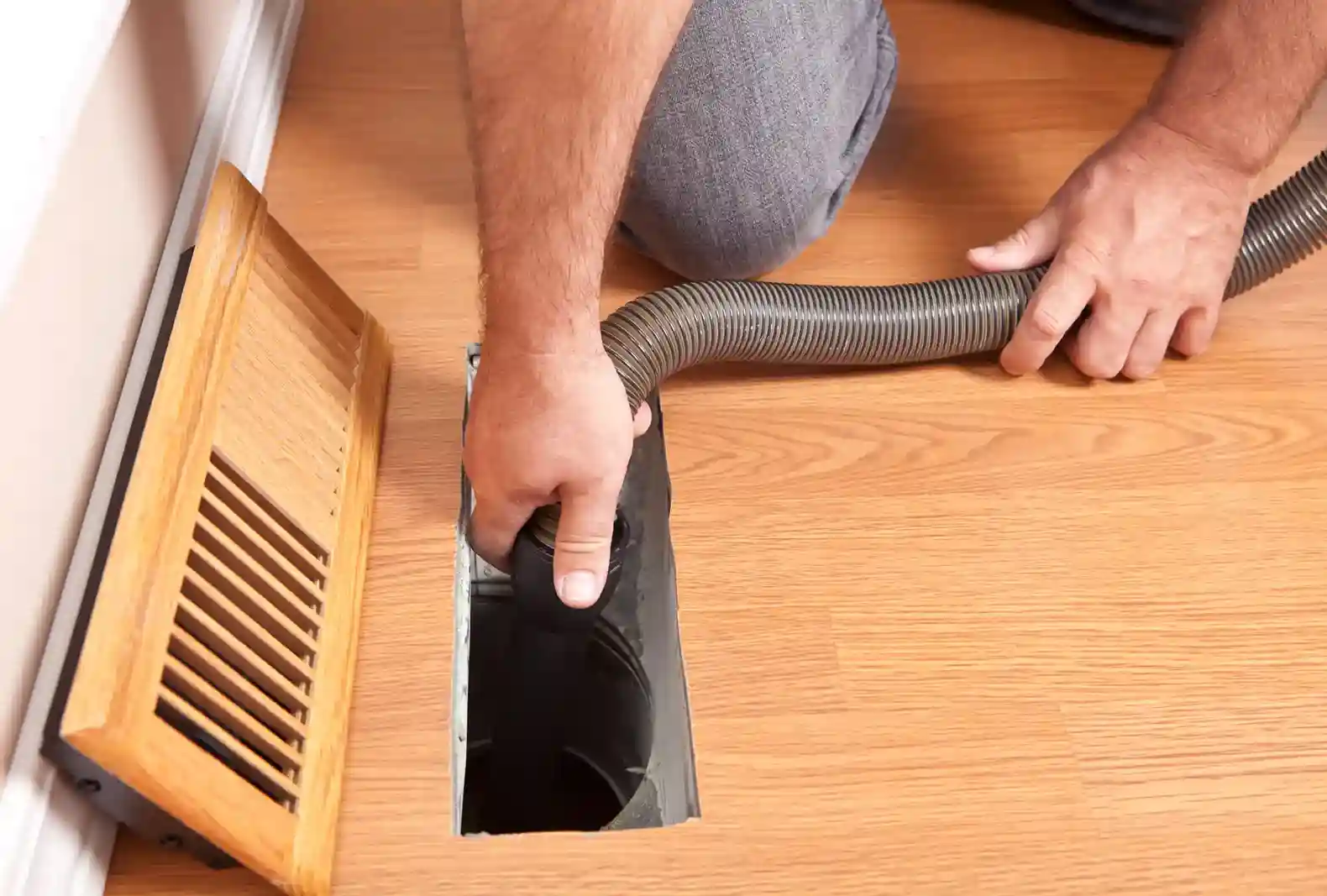 Technician cleaning a home air duct vent with a professional vacuum hose
