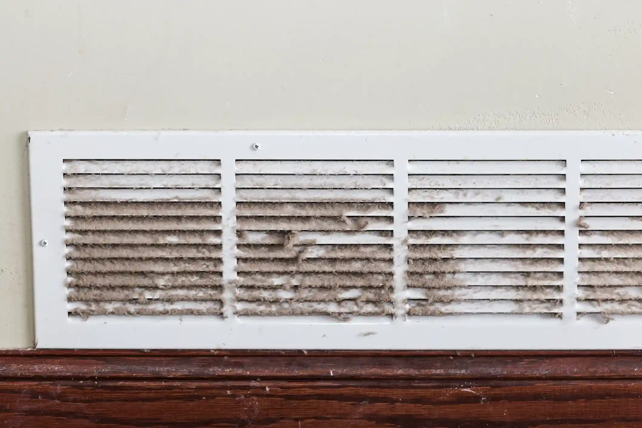 A dirty white air vent covered in a thick layer of dust and lint on a wall.