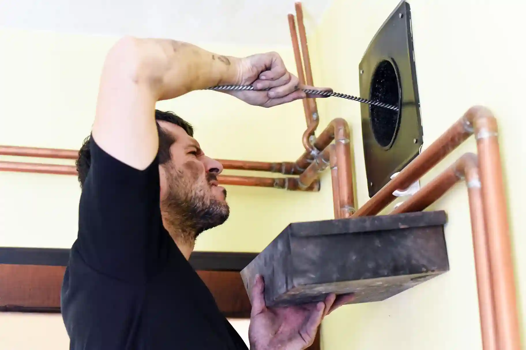 Technician cleaning an indoor boiler flue or cleanout with a long, thin wire brush.