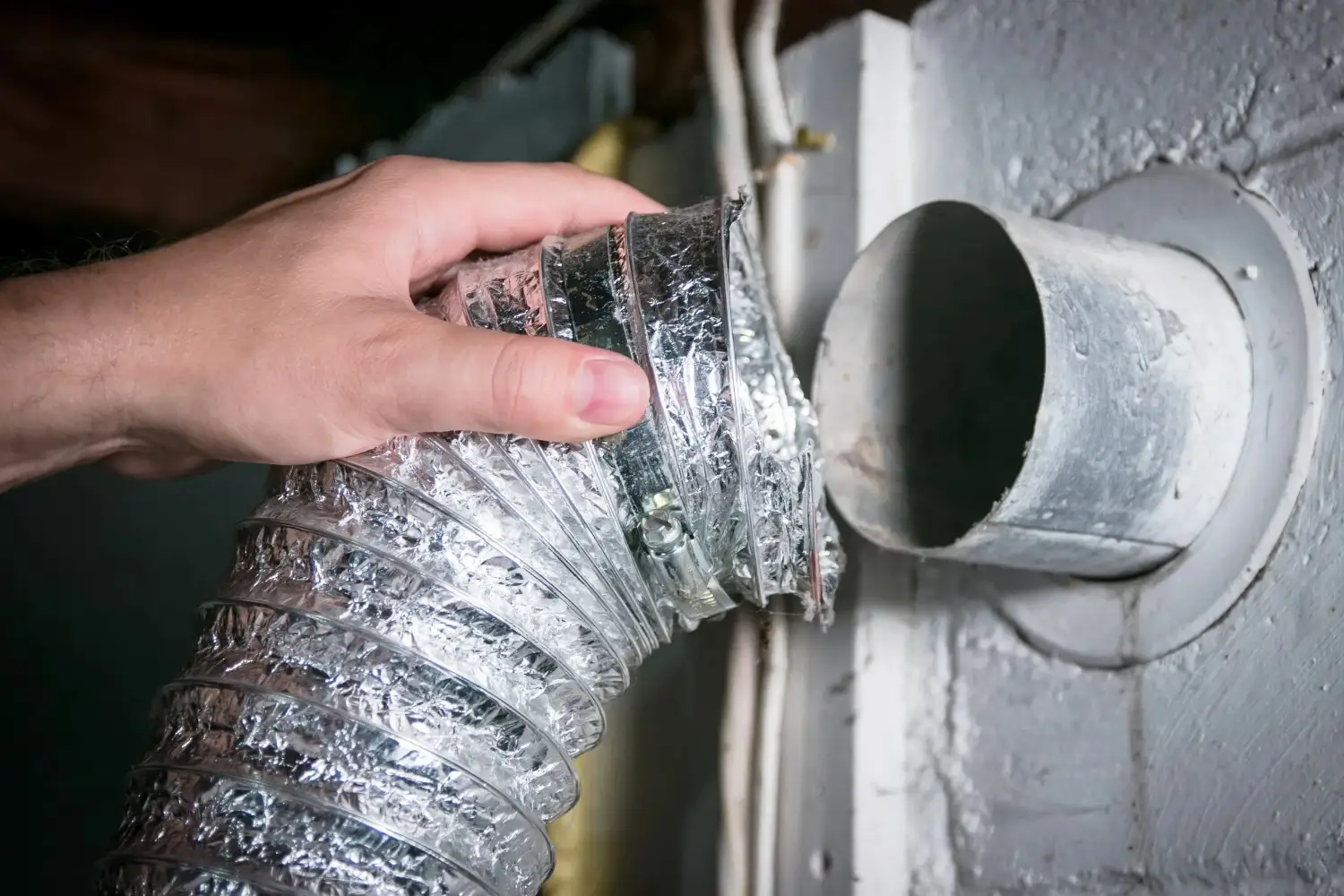 A hand attaches a clean, flexible metal dryer duct to a wall vent