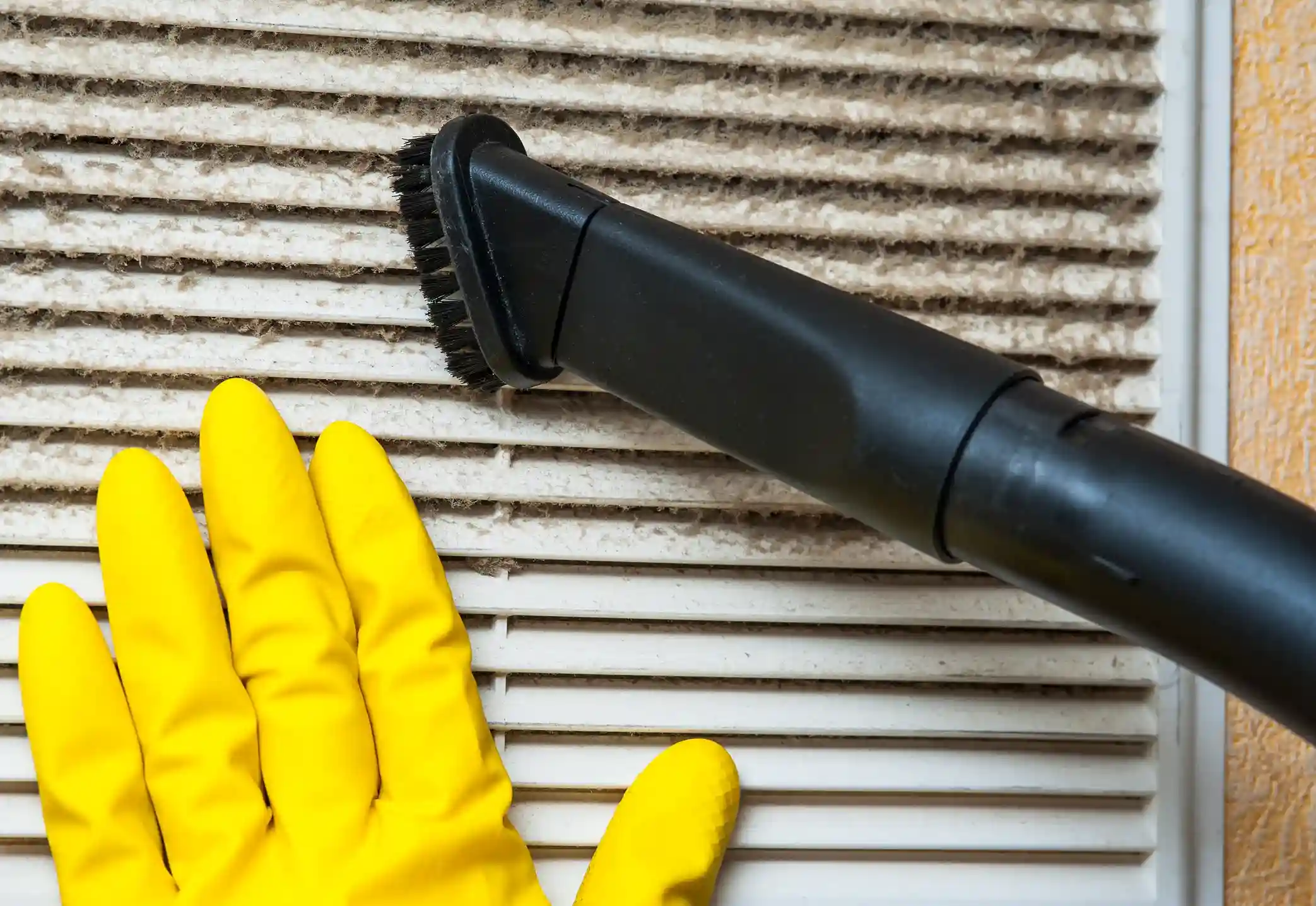 Close-up of vacuum brush attachment cleaning heavy dust from a dirty air ventilation grille.