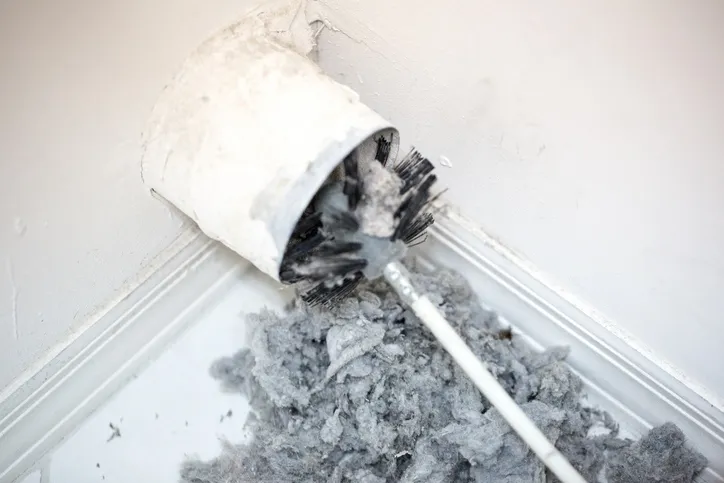 A long, round brush covered in dust is being pulled out of a dusty air duct.