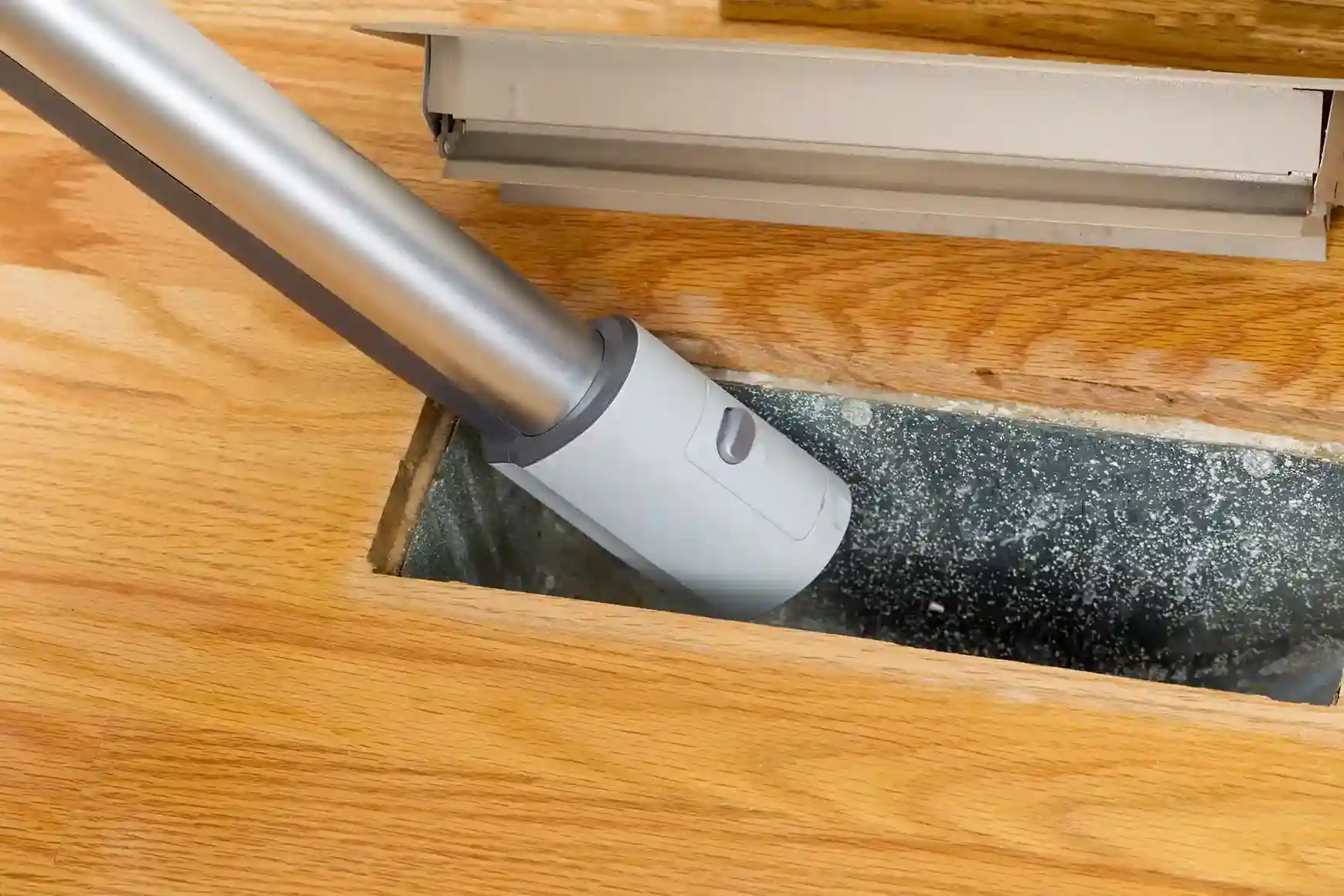 Vacuum hose cleaning visible dust and debris from an open floor air duct vent.